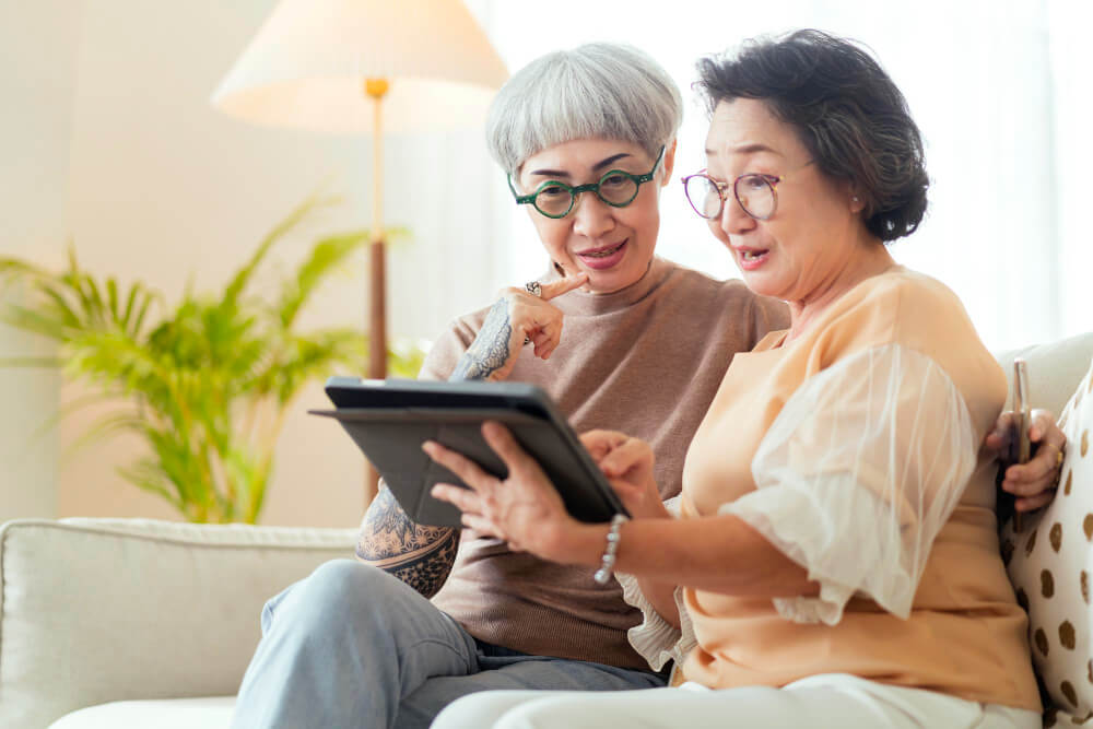 visit house two senior old mature female friends looking through old photos digital album together with tablet device sofa living room home old friend spending quality time together